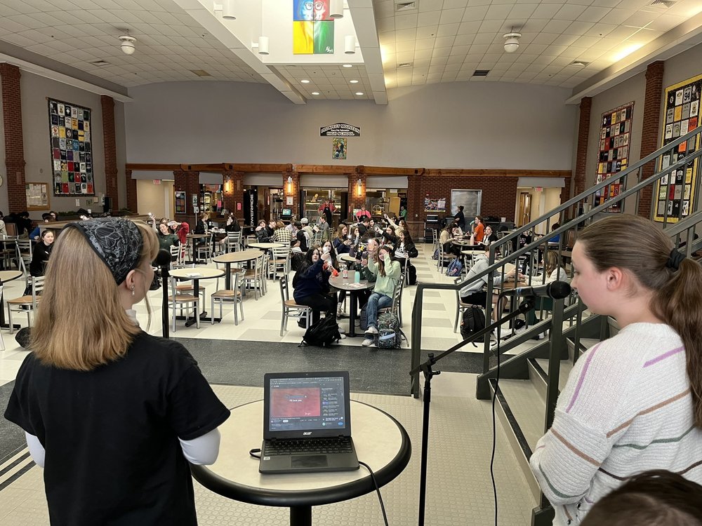 Two students singing into microphone in front of a crowd of students